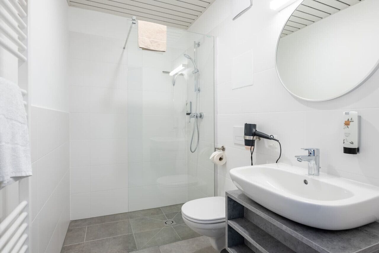 Ein modernes Badezimmer mit einer gläsernen Duschkabine, einem weißen Waschbecken und einer Toilette.