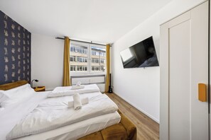 Ein Hotelzimmer mit Bett, Fernseher, Fenster mit Vorhängen und Blick auf Gebäude.