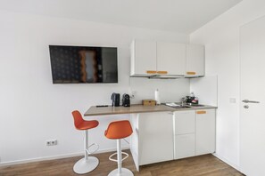 A compact kitchen with white cabinets, a wooden countertop, and two orange bar stools. - Arbio I Cube Apartments (Hamburg)