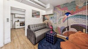 A modern living space with a grey sofa, a blue side table, and a colorful brick-patterned wall. - Arbio I Cube Apartments (Hamburg)