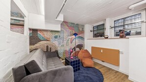 A modern living space with a grey sofa, a colorful abstract mural, a blue floor lamp, and a wooden radiator. - Arbio I Cube Apartments (Hamburg)
