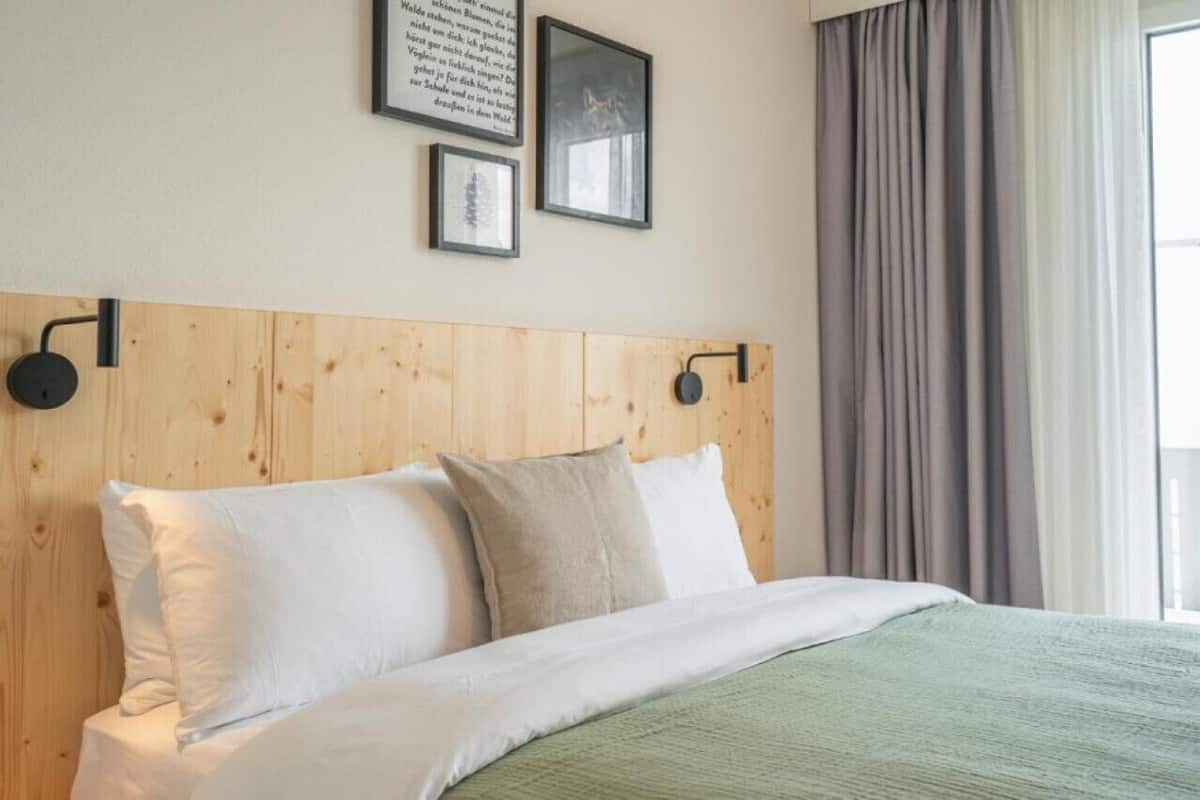 Ein ordentlich bezogenes Bett mit weißen und beige farbenen Kissen, einem Holzkopfschild und einer grünen Decke.