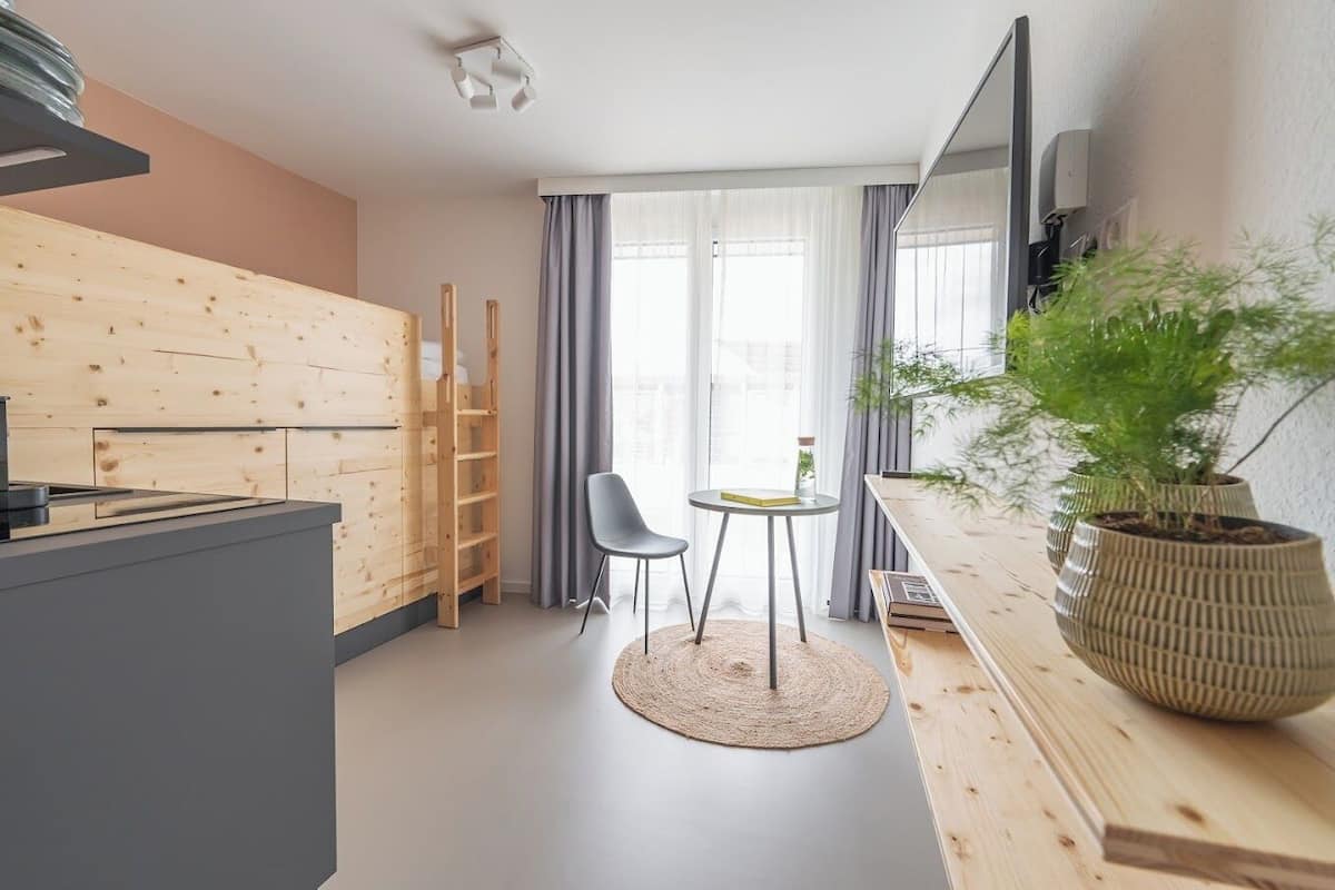 Eine moderne Küche mit Holzschränken, ein Essbereich mit einem kleinen Tisch und zwei Stühlen sowie eine große Kübelpflanze.