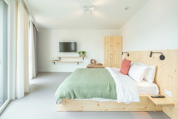 A modern bedroom with a wooden bed, a mounted TV, and a bedside table with a lamp.
