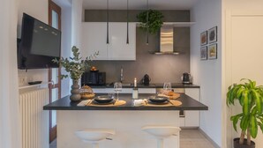 Eine moderne Küche mit einer zentralen Kochinsel, weißen Barhocker, Pendelleuchten und einem Blumentopf.
