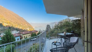 Ein Balkon mit Tisch und Stühlen mit Blick auf ein malerisches Tal mit Häusern und einem See.