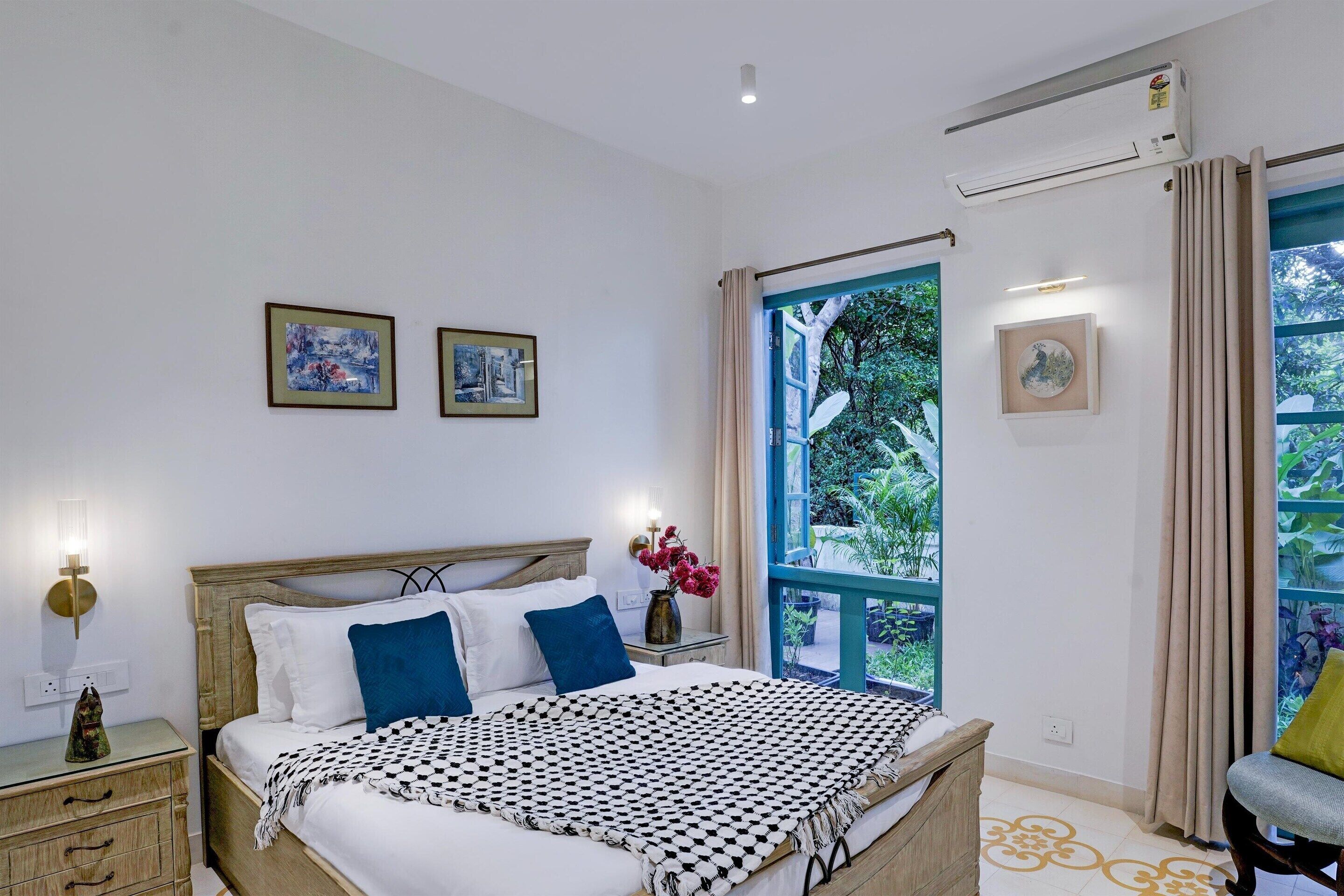 A bedroom with a bed, bedside tables, a window with curtains, and wall-mounted artwork.
