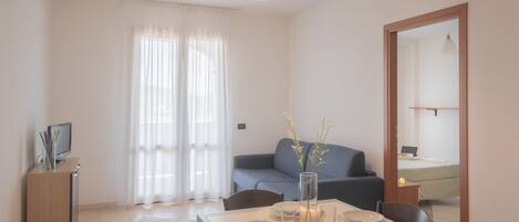 Un coin repas avec une table dressée pour quatre personnes, un canapé et un téléviseur posé sur un meuble.