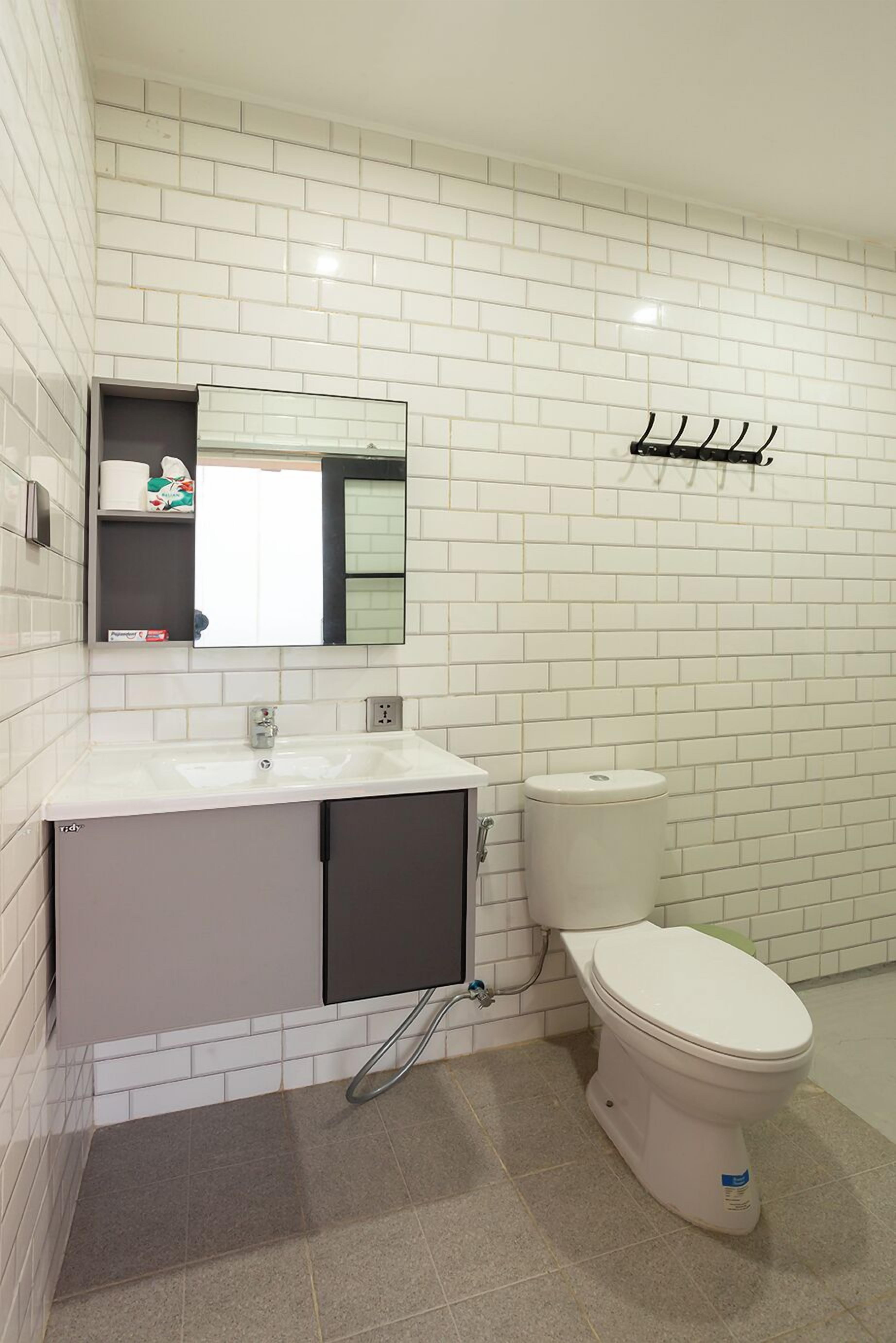 A bathroom with white tiled walls, a white sink, a toilet, and a mirror above the sink.