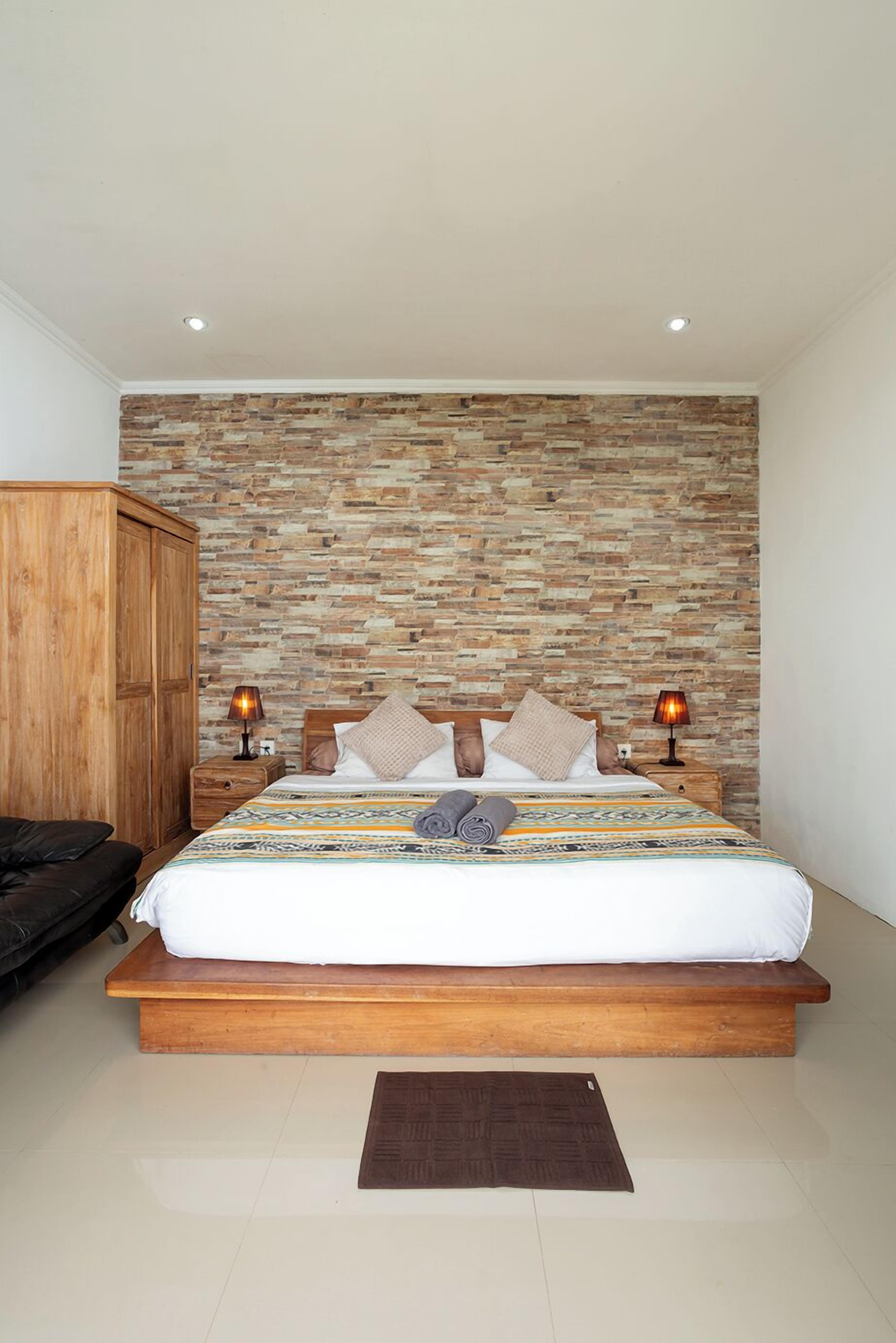 A bedroom with a stone-patterned wall, a wooden bed frame, two bedside lamps, and a brown rug.