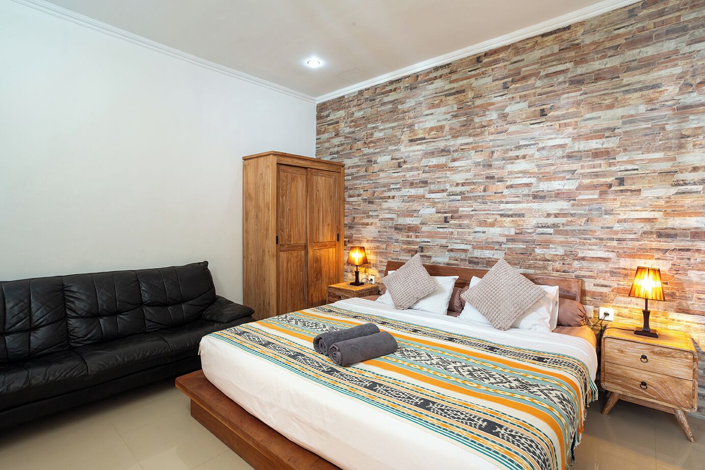 Una camera da letto con un letto, un armadio in legno, un divano nero e due comodini con lampade.