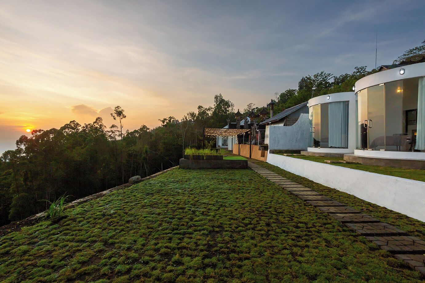 A modern house with a large glass facade, a well-maintained lawn, and a view of the sunset.
