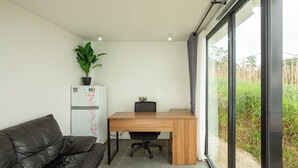 A compact living space with a wooden desk, a black leather couch, a refrigerator with magnets, and a potted plant. - Alam Nirwana Kintamani (Kintamani)