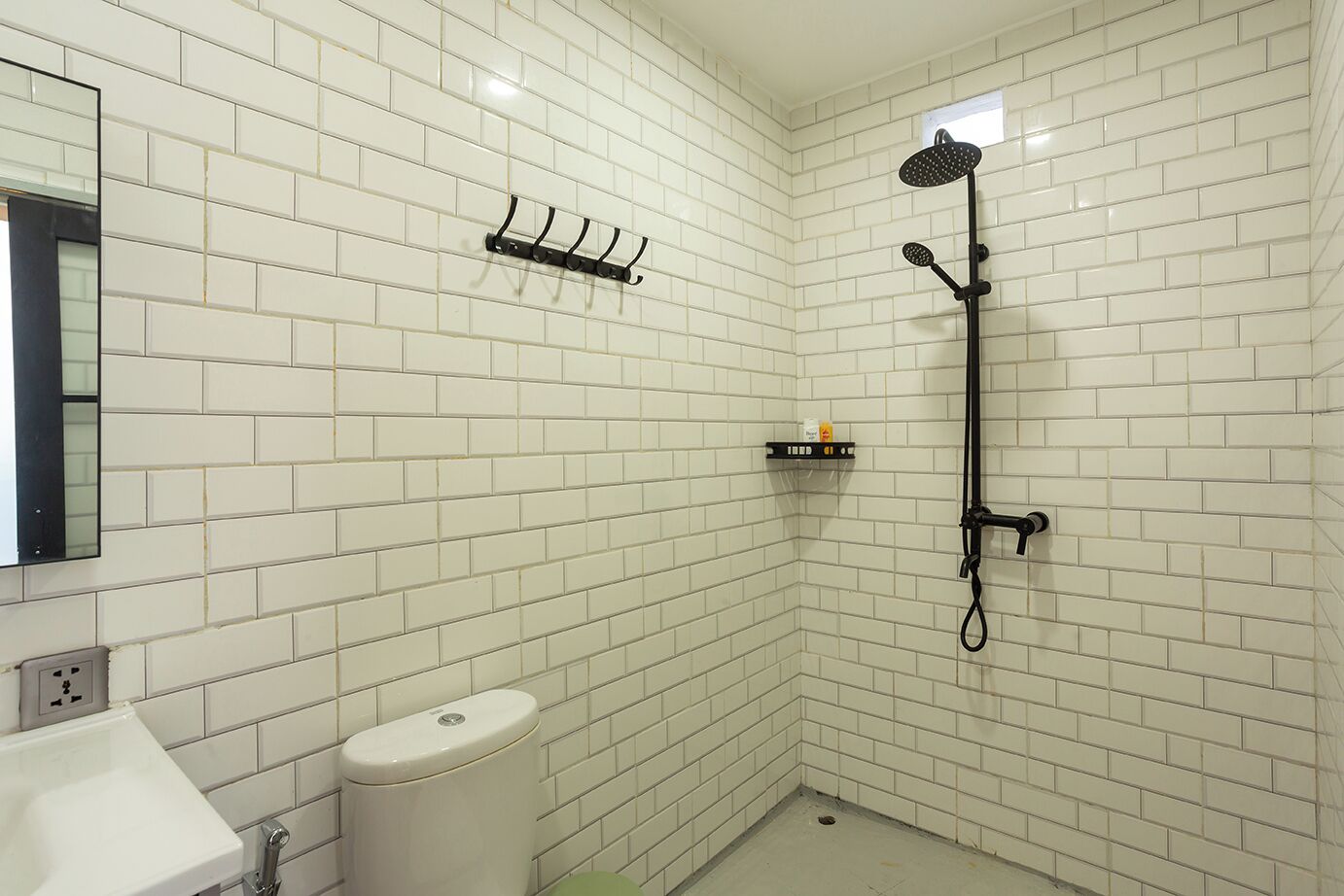 A small, white-tiled bathroom with a toilet, sink, and a shower with a handheld showerhead.
