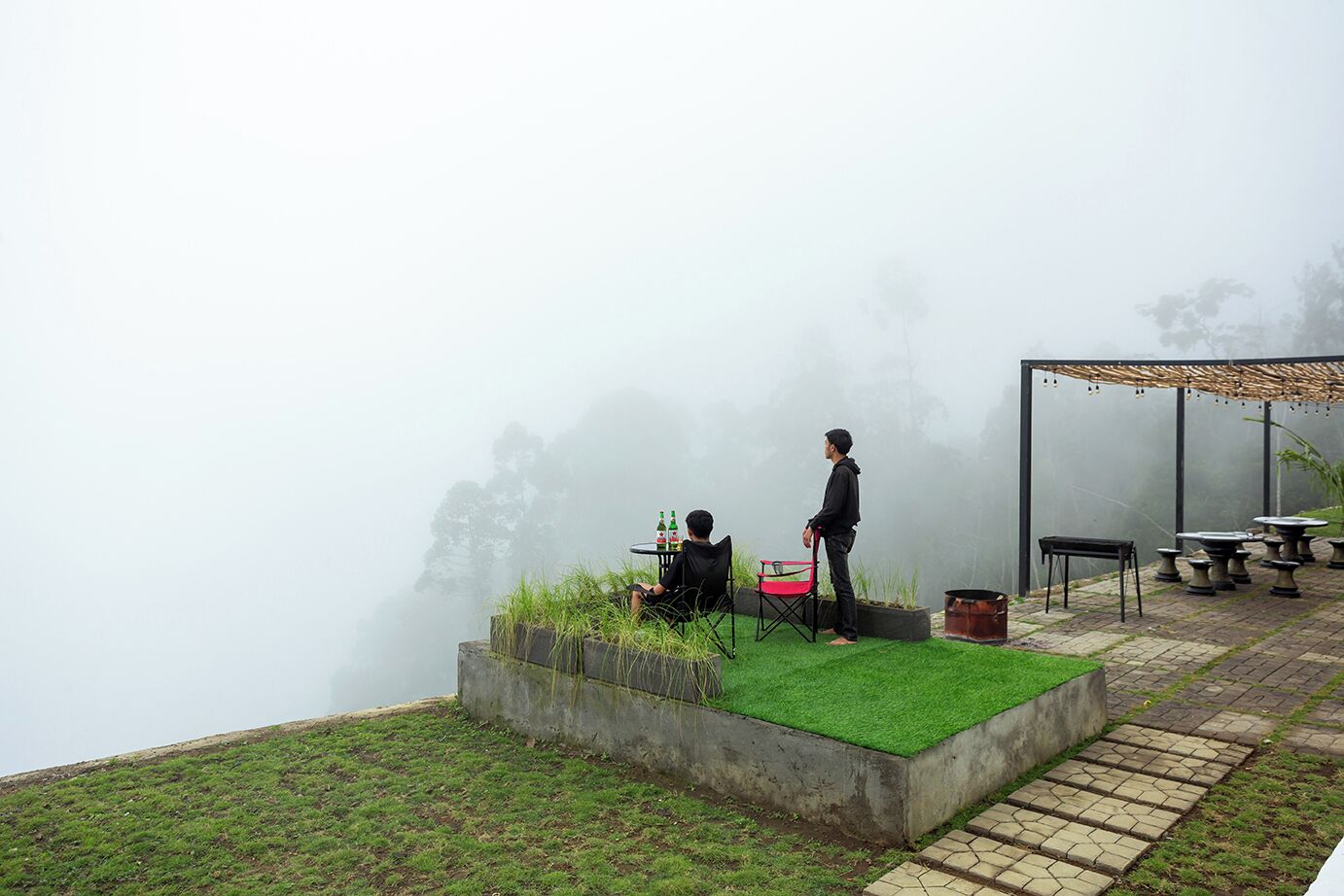 A foggy outdoor seating area with tables and chairs, a person standing, and a view of trees in the background.