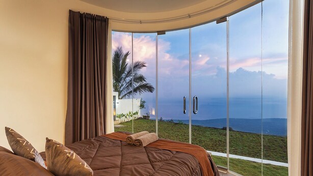 A bedroom with a large bed, a view of the sea, and a balcony with a glass door. - Alam Nirwana Kintamani (Kintamani)