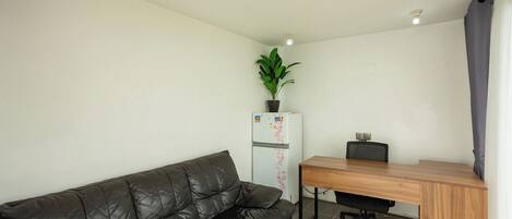 A compact living space with a black leather sofa, a wooden desk, and a white refrigerator with magnets.
