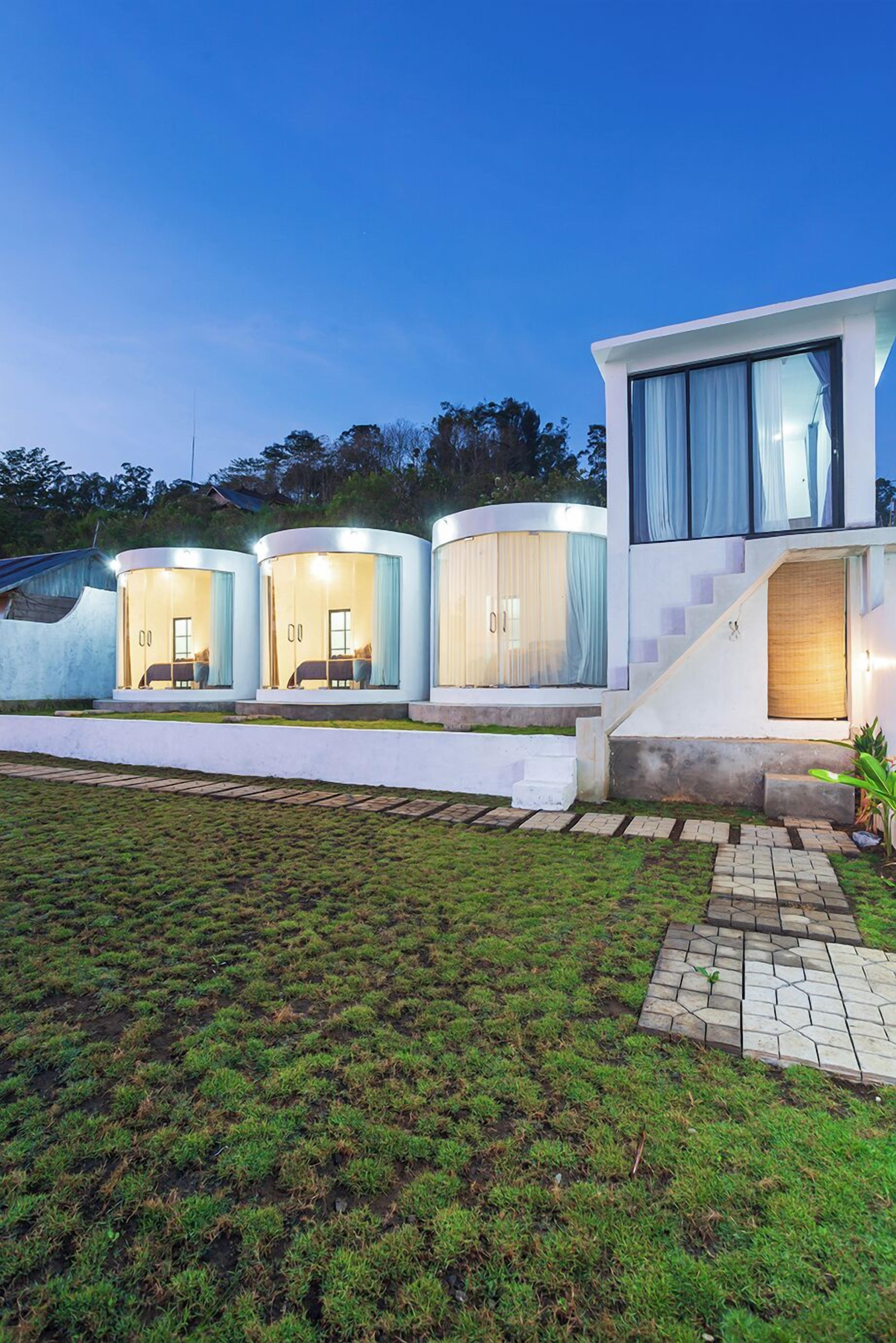 A modern building with three cylindrical guest rooms, each with a bed and a window.