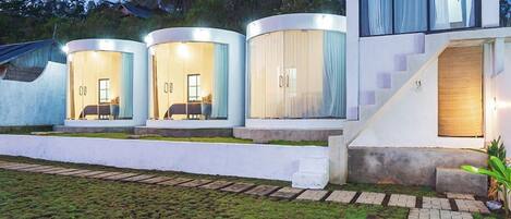 A modern building with three cylindrical guest rooms, each with a bed and a window.