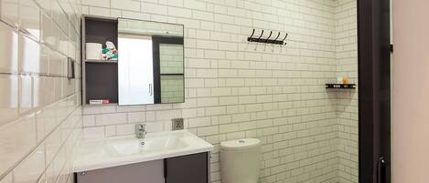 A modern bathroom with white subway tiles, a white sink, a toilet, and a mirror above the sink.