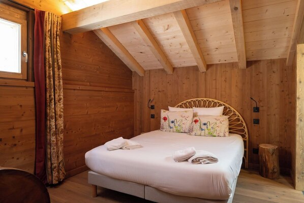 A wooden room with a bed, curtains, and a window.