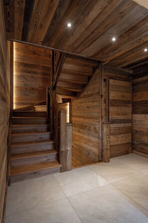 A wooden staircase leading to a lower level, with a tiled floor and a wooden door at the bottom.