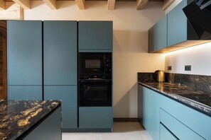 A modern kitchen with teal cabinetry, a black oven, and a marble countertop.