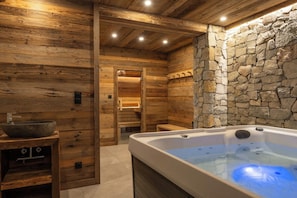 A wooden interior with a stone wall, a wooden bench, and a hot tub. - L'Aiglon - 10 pers - Jacuzzi + Sauna (Gérardmer)
