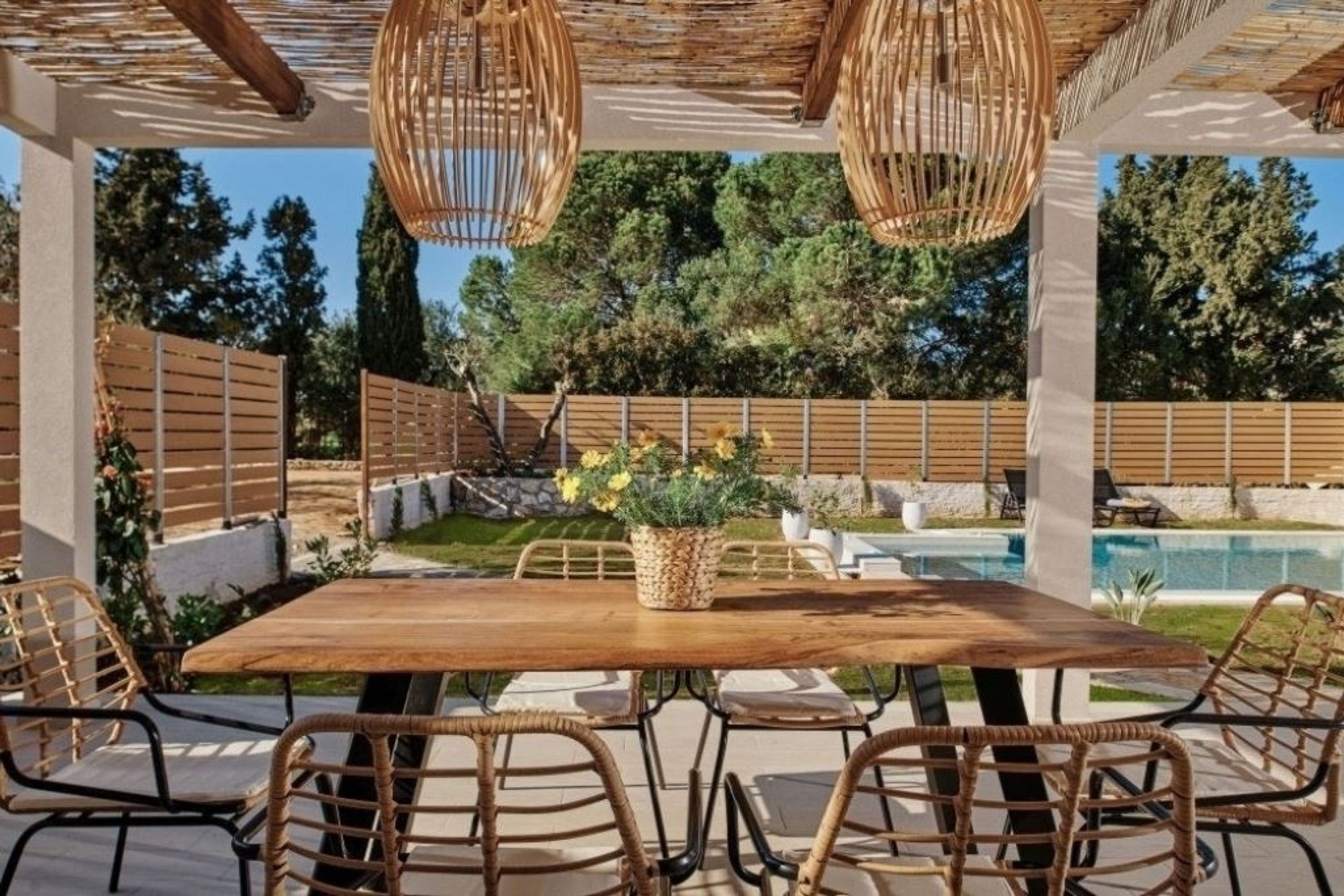 Eine Terrassenanlage im Freien mit Holztisch und Korbstühlen, umgeben von einem Holzzaun und einem Pool.