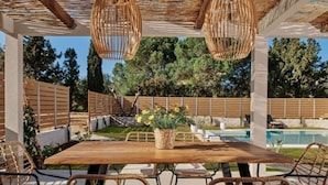 An outdoor patio with a wooden table and wicker chairs, surrounded by a wooden fence and a pool. - Villa Danae Periyali (Zakynthos)