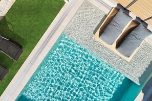 An aerial view of a swimming pool with clear water, surrounded by a tiled deck and a grassy area.