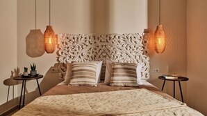 A bedroom with a decorative headboard, two bedside tables, a bed with patterned bedding, and hanging lamps. - Villa Danae Periyali (Zakynthos)