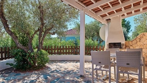 An outdoor patio with stone flooring, wicker furniture, and a stone fireplace. - Villa Cleo Periyali (Zakynthos)