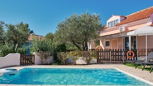 A swimming pool with a tiled deck, a wooden fence, and a building with a tiled roof in the background. - Villa Cleo Periyali (Zakynthos)