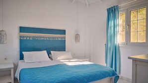 A bedroom with a bed, white nightstands, a blue headboard, and a window with curtains. - Villa Cleo Periyali (Zakynthos)