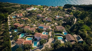 An aerial view of a coastal residential area with multiple houses, each with a swimming pool, surrounded by greenery and the sea. - Villa Lito Periyali (Zakynthos)