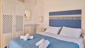 A neatly made bed with blue bedding and white pillows, a bedside table with a lamp, and a wardrobe with patterned doors. - Villa Lito Periyali (Zakynthos)
