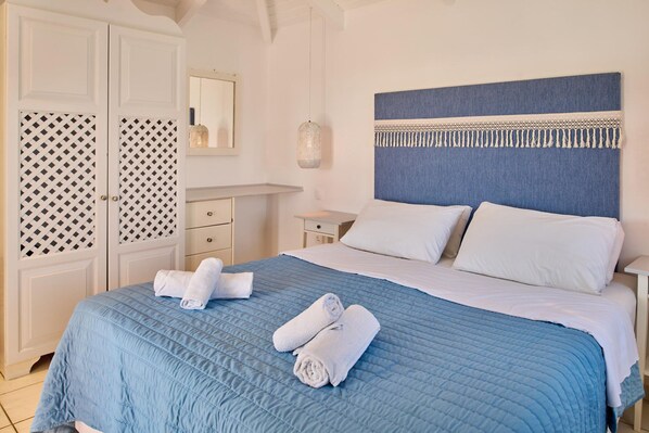 A neatly made bed with blue bedding and white pillows, a bedside table with a lamp, and a wardrobe with patterned doors. - Villa Lito Periyali (Zakynthos)