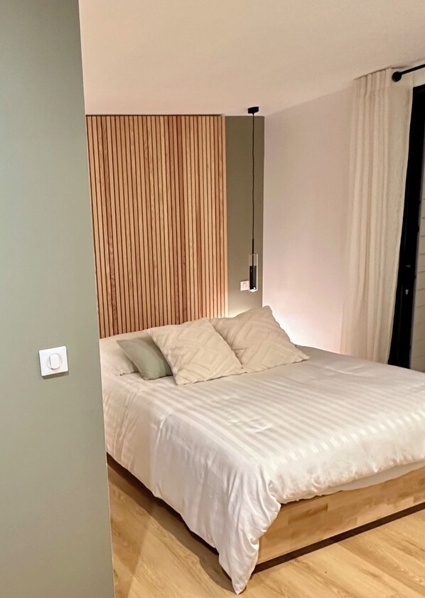 A modern bedroom with a wooden slat headboard, a bed with white bedding, and a bedside table with a lamp.