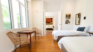 Un dormitorio con dos camas, suelo de madera, un escritorio con sillas y vistas a un jardín a través de amplios ventanales.