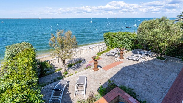 Un patio frente al mar con sillones, una maceta decorativa y vistas al océano con barcos.