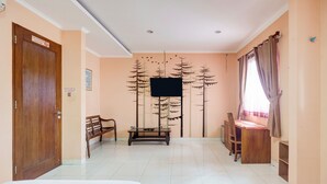 Une chambre d’hôtel avec deux lits, un bureau en bois, un banc, un téléviseur fixé au mur et une fenêtre avec des rideaux.
