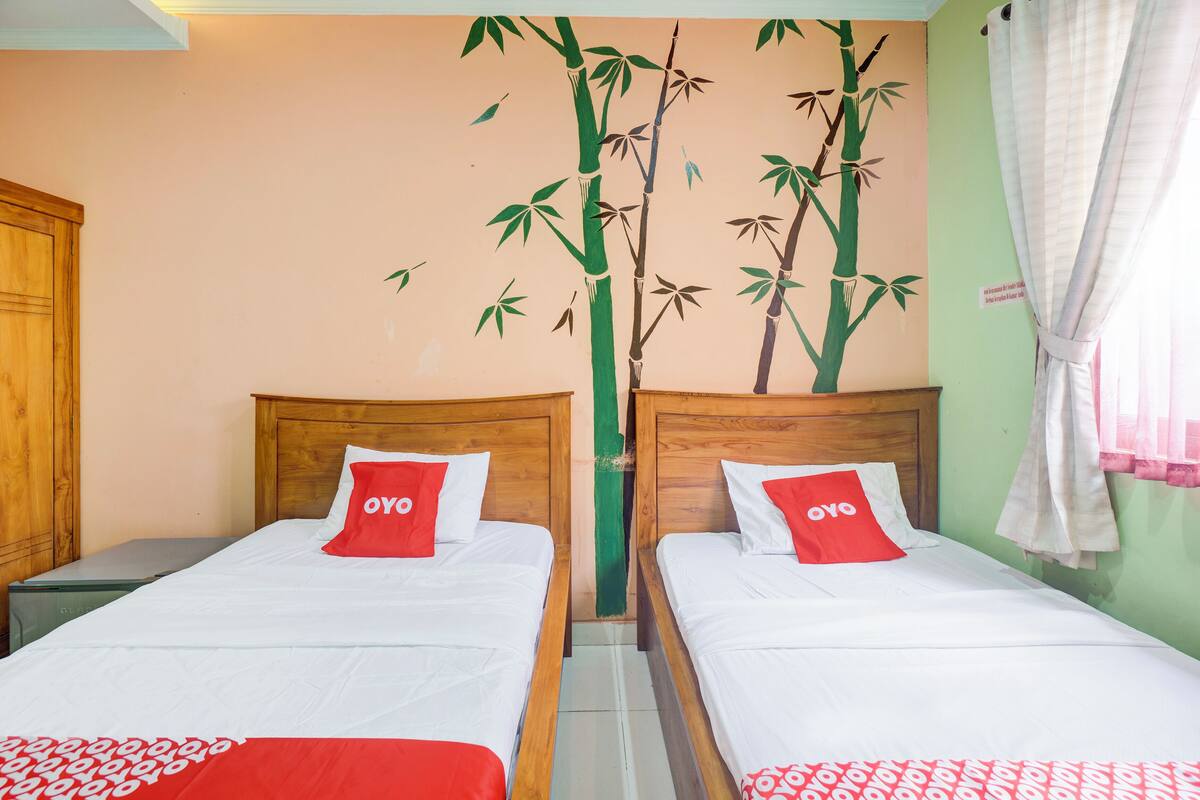 Une chambre avec deux lits, chacun doté d’une tête de lit en bois et d’un oreiller rouge orné du logo « OYO ».