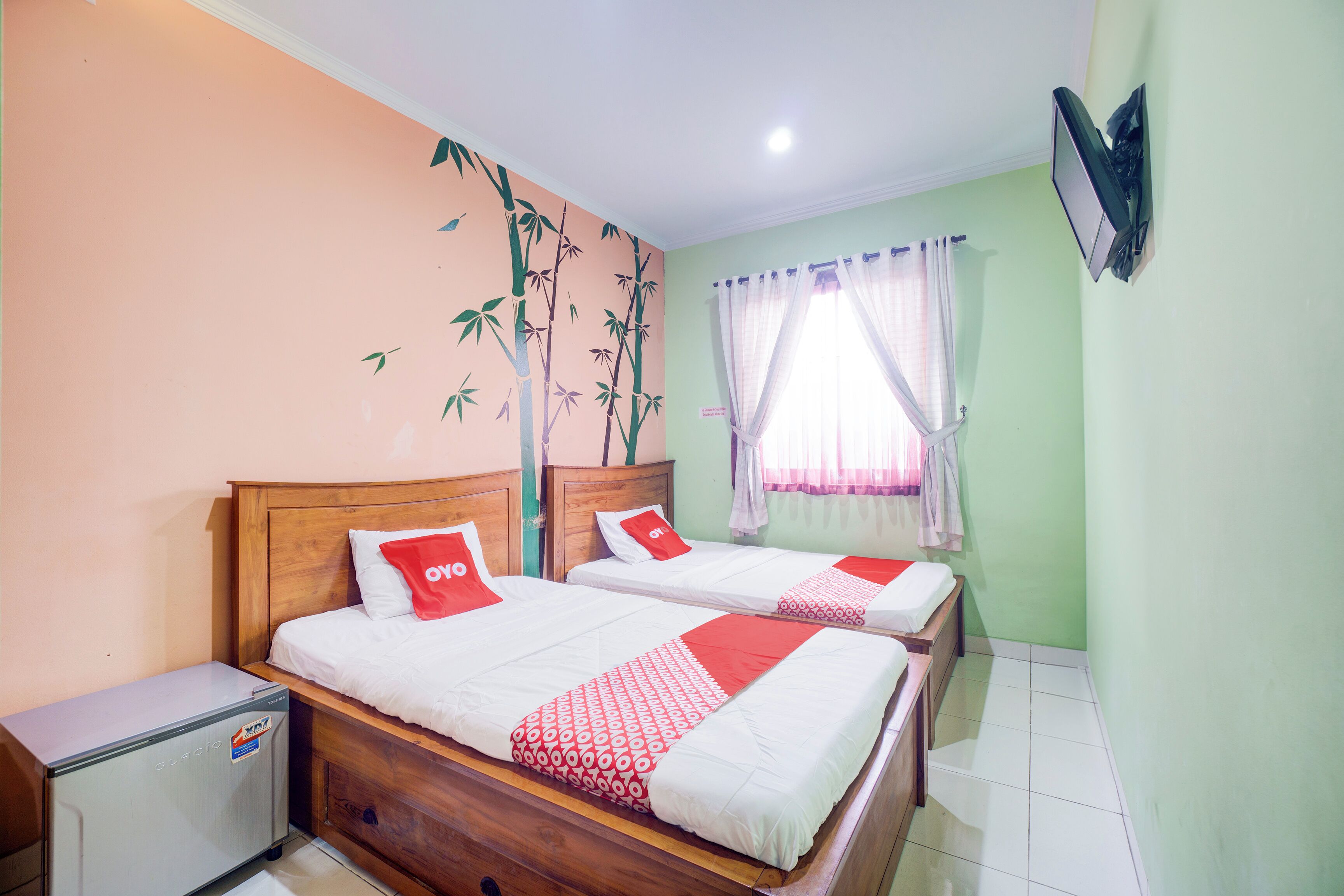 Habitación de hotel con dos camas, un refrigerador pequeño y una ventana con cortinas.
