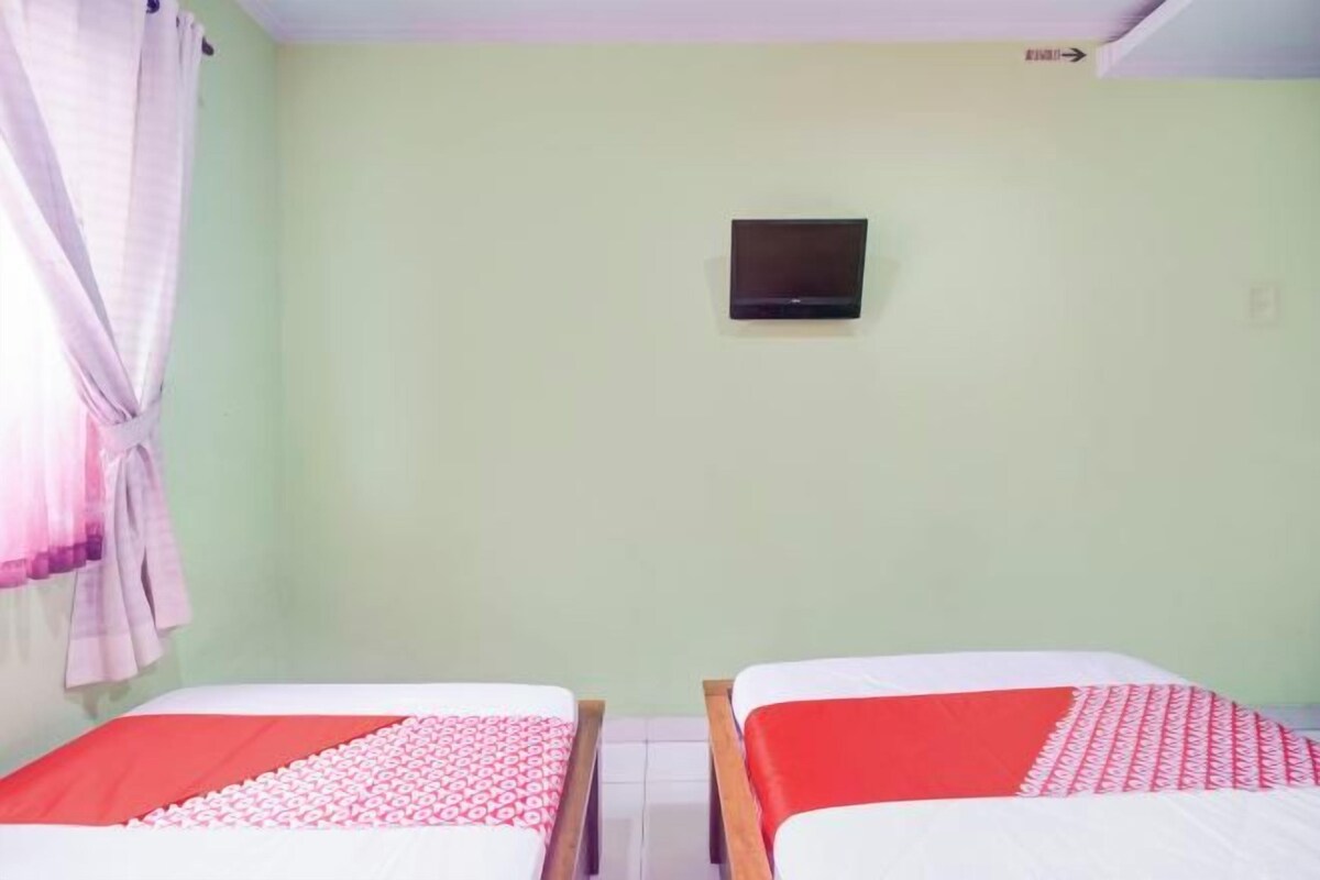 Una habitación con dos camas, un televisor en la pared y una cortina a la izquierda.