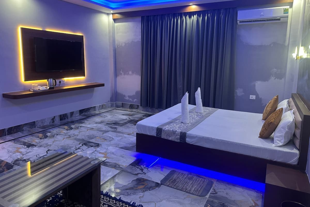 A modern bedroom with a large bed, a flat-screen TV mounted on the wall, and a ceiling fan.