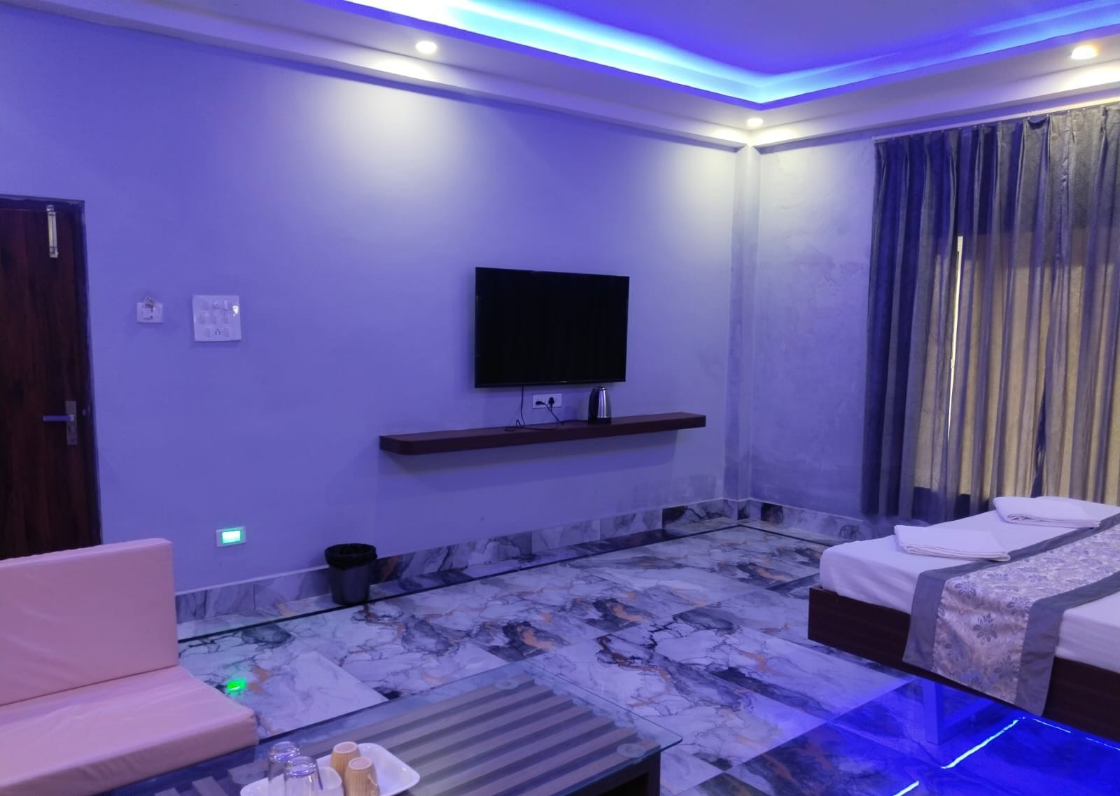 A modern hotel room with a flat-screen TV, a sofa, a bed, and a marble-patterned floor.