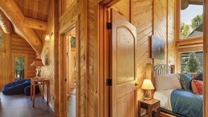 Interior de una cabaña de madera con cama, mesita de noche, lámpara y un sillón de peluche azul.