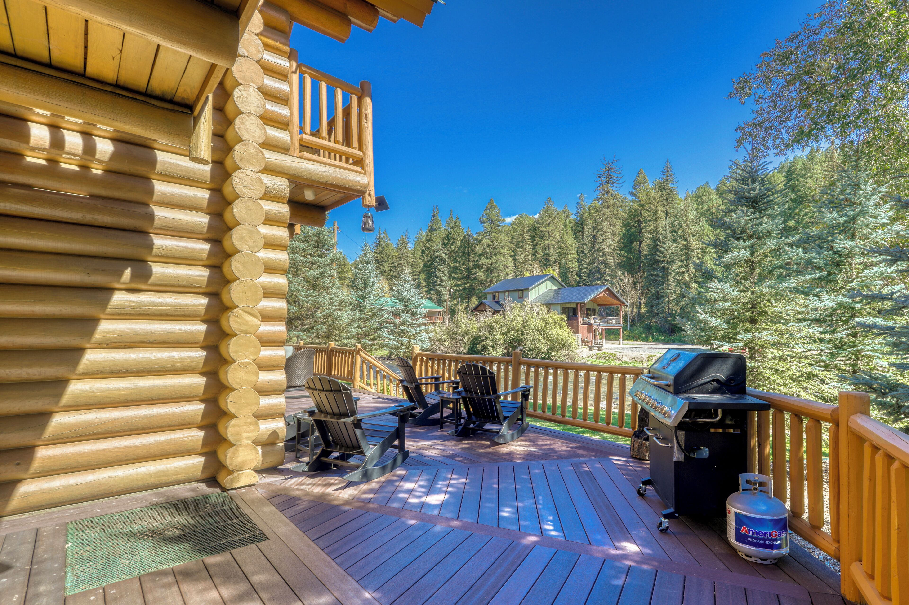 Una terraza de madera con mobiliario exterior y una parrilla, con vistas a una zona boscosa.