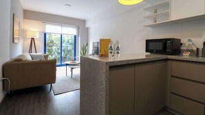 A modern kitchen with a built-in microwave, a small island, and a dining area with a sofa and a lamp. - w* | Bright 1BR in Historic Cusco w/ Balcony (Cusco)